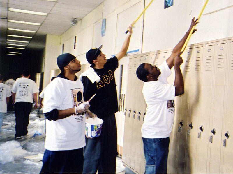 volunteers in a school hallway using poles for repairs near a ceiling 